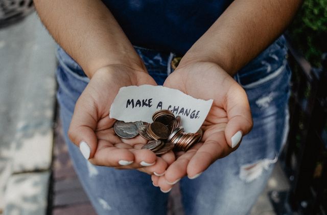 Cupped hands holding coins and a scrap of paper reading 'Make a change'