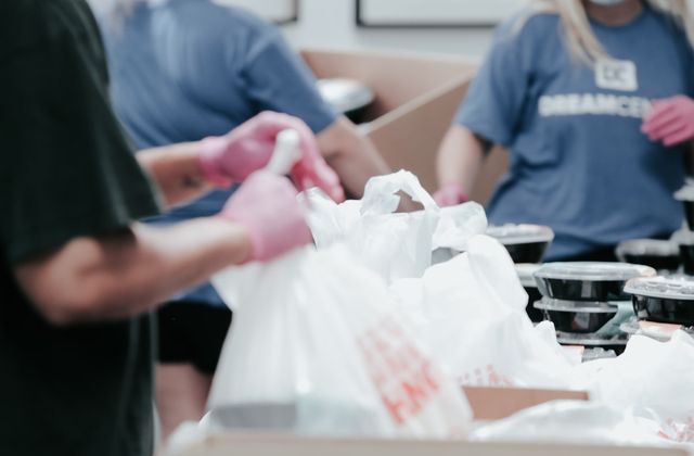 Volunteers in gloves packing food parcels into white carrier bags
