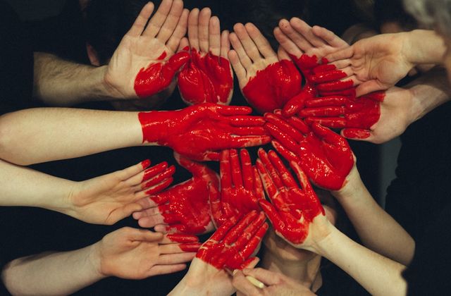 A circle of outstretched hands with red-painted palms forming a heart
