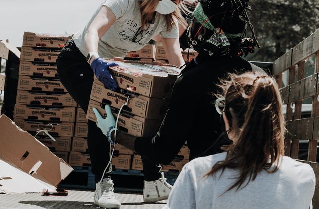 Volunteers in gloves and masks unloading boxes of food from a truck