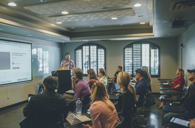 A speaker presenting slides to a seated audience in a training room