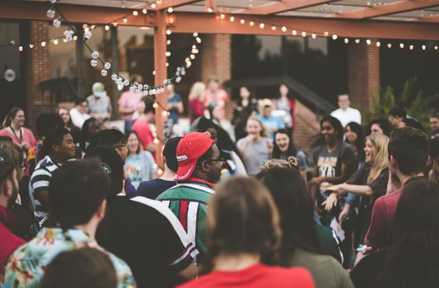 A crowd of people chatting at an outdoor evening gathering under string lights