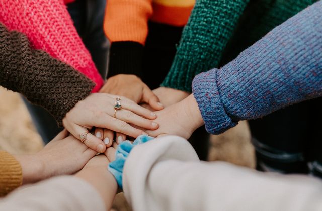 Several people in knitted jumpers stacking their hands together in the middle