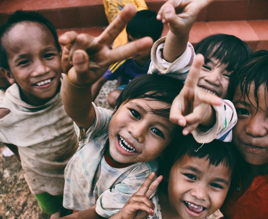A group of smiling children crowding towards the camera, some making peace signs