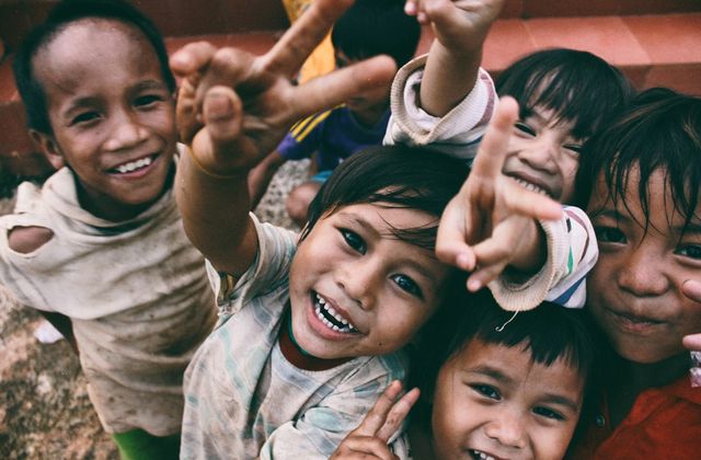 A group of smiling children crowding towards the camera, some making peace signs